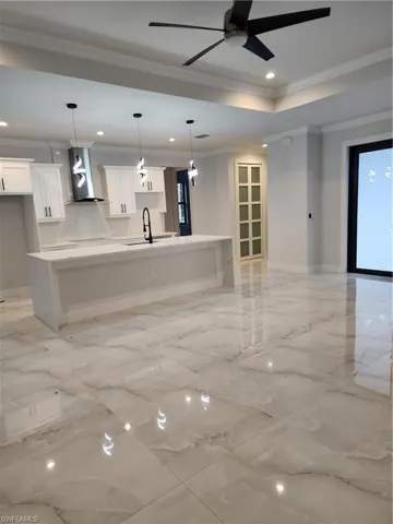 Kitchen with a large island with sink, open floor plan, recessed lighting, wall chimney exhaust hood, and light stone countertops