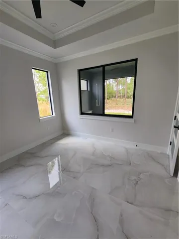 Empty room featuring ornamental molding, a tray ceiling, and marble finish flooring