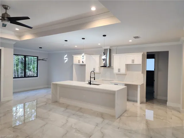 Kitchen featuring light stone countertops, ceiling fan, an island with sink, light marble finish flooring, and white cabinets