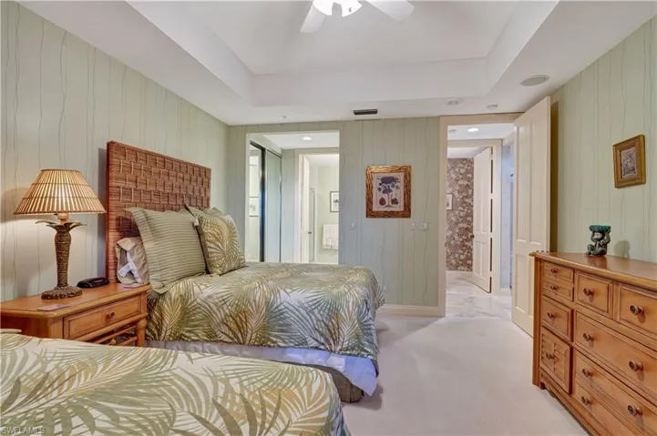 Carpeted bedroom with wooden walls, ensuite bath, ceiling fan, and a tray ceiling