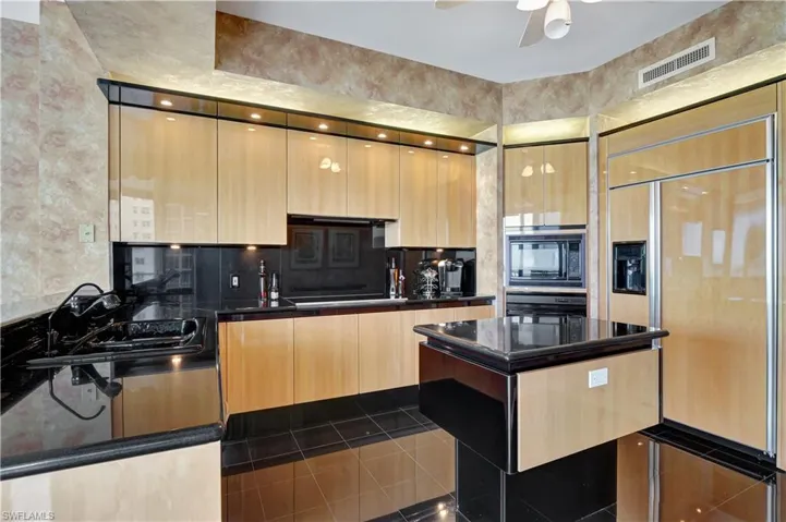 Kitchen featuring black appliances, tasteful backsplash, light brown cabinetry, sink, and dark stone countertops