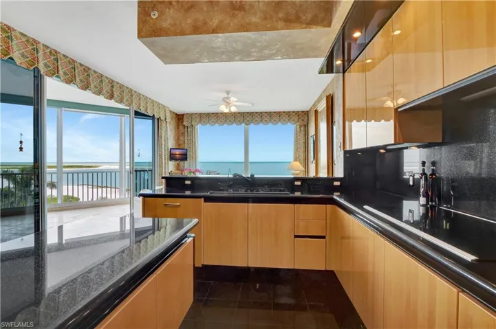 Kitchen featuring ceiling fan, dark tile patterned flooring, sink, dark stone counters, and black stovetop