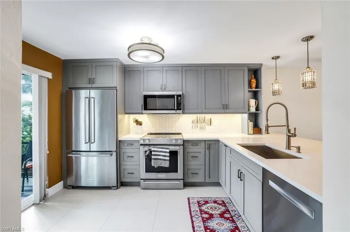 Kitchen featuring stainless steel appliances, gray cabinetry, light stone counters, open shelves, and a breakfast bar