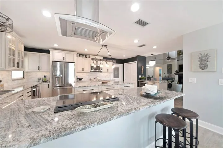 Kitchen featuring a peninsula, range hood, hanging light fixtures, stainless steel appliances, and decorative backsplash