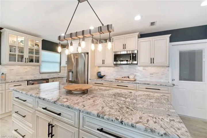 Kitchen with light wood-style flooring, appliances with stainless steel finishes, glass insert cabinets, tasteful backsplash, and light stone counters