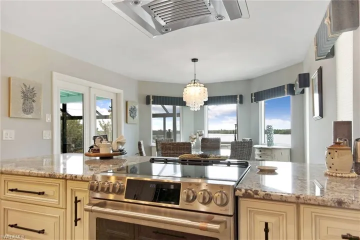 Kitchen featuring stainless steel range with electric stovetop, light stone countertops, exhaust hood, and healthy amount of natural light