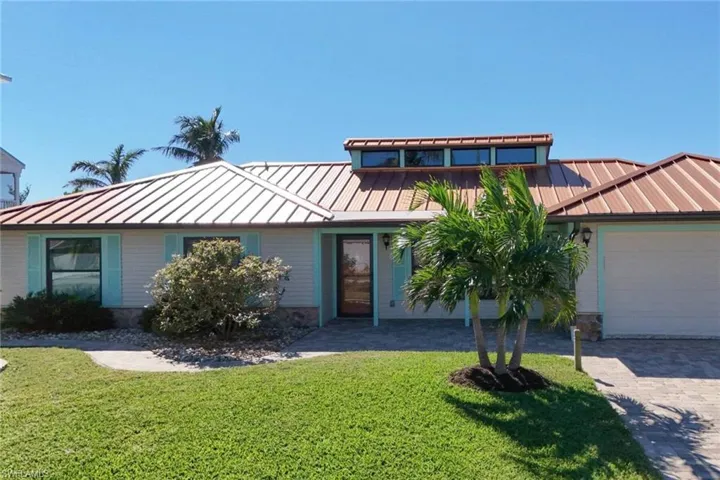 View of front facade with a standing seam roof, a metal roof, a front lawn, and a garage