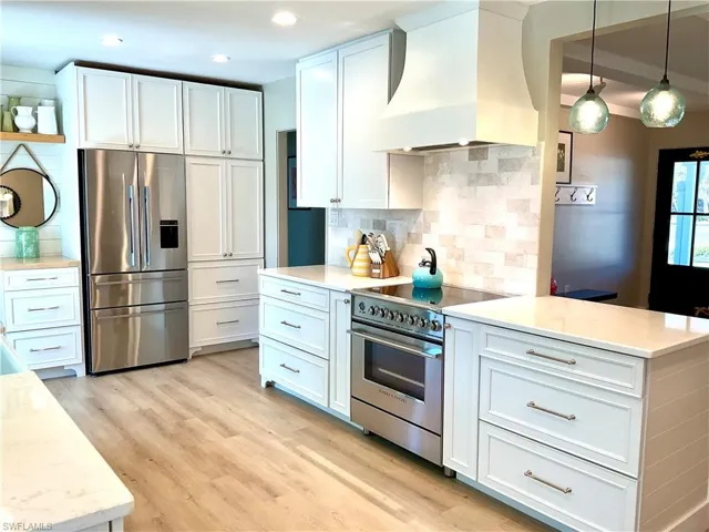 Kitchen featuring premium range hood, stainless steel appliances, white cabinets, light wood-style floors, and decorative light fixtures