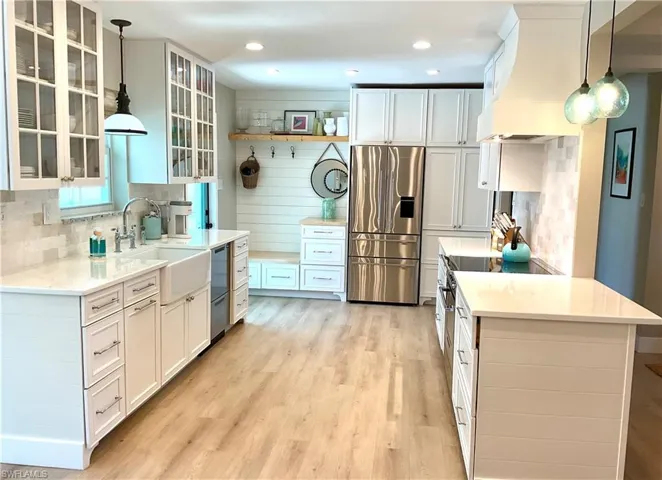 Kitchen with hanging light fixtures, stainless steel appliances, custom range hood, white cabinets, and recessed lighting
