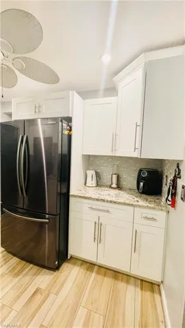 Kitchen with ceiling fan, light hardwood / wood-style floors, backsplash, white cabinets, and stainless steel refrigerator
