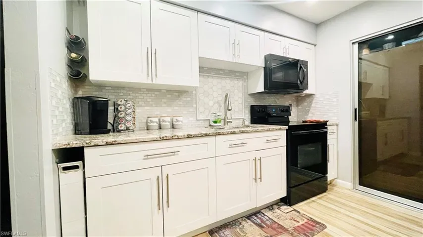 Kitchen with white cabinetry, light stone countertops, light wood-type flooring, black appliances, and backsplash