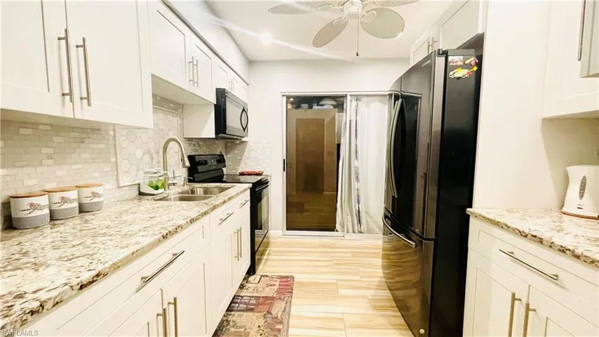 Kitchen featuring ceiling fan, tasteful backsplash, black appliances, light stone counters, and white cabinetry