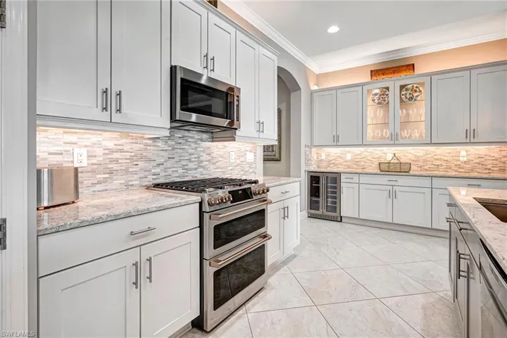 Kitchen featuring appliances with stainless steel finishes, light stone counters, wine cooler, decorative backsplash, and ornamental molding