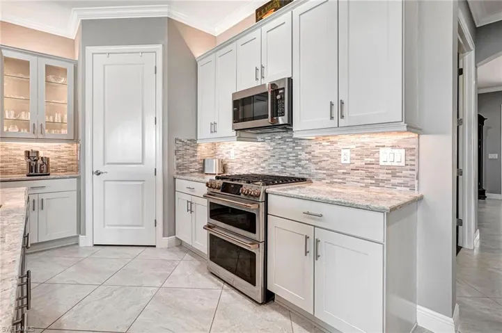 Kitchen with white cabinetry, light stone counters, stainless steel appliances, and backsplash