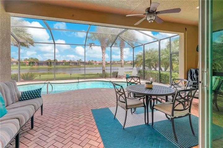 View of pool with a water view, glass enclosure, ceiling fan, and a patio