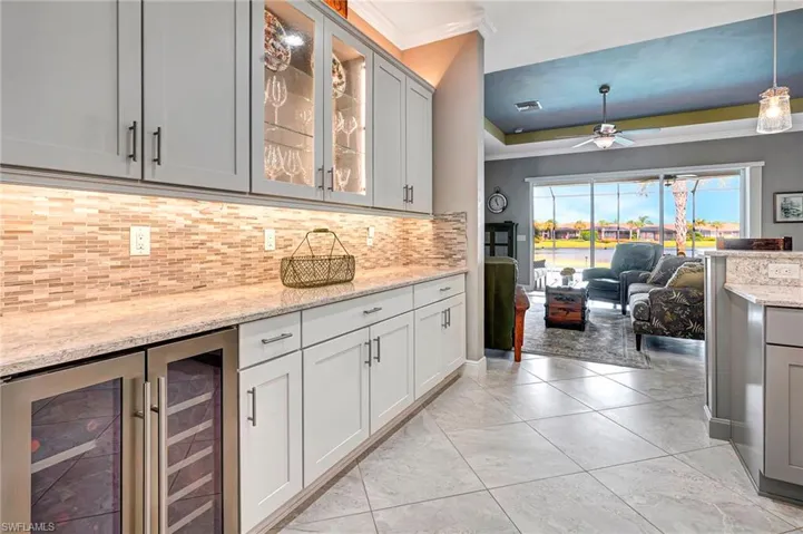 Kitchen featuring decorative light fixtures, light stone counters, beverage cooler, decorative backsplash, and ornamental molding