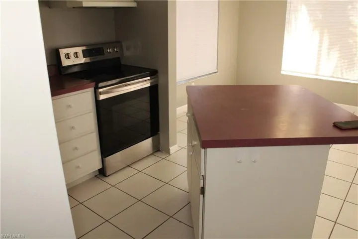Kitchen featuring dark countertops, stainless steel electric stove, white cabinetry, light tile patterned flooring, and a center island