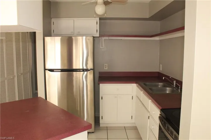 Kitchen with freestanding refrigerator, dark countertops, electric range, white cabinets, and ceiling fan