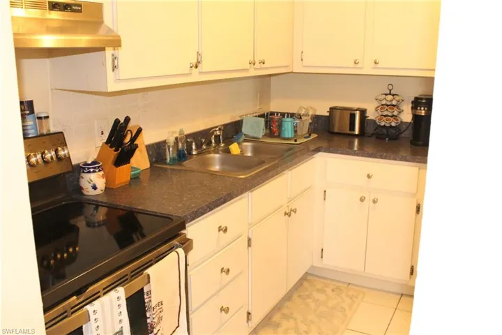 Kitchen with stainless steel range with electric cooktop, dark countertops, under cabinet range hood, white cabinetry, and light tile patterned floors