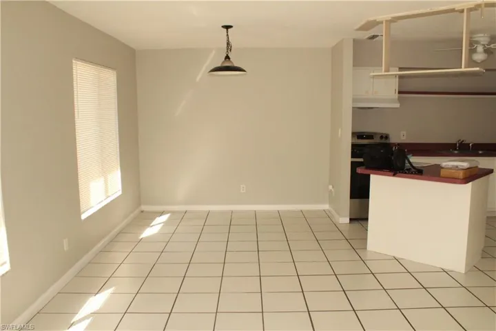 Kitchen with electric stove, pendant lighting, white cabinetry, and light tile patterned flooring