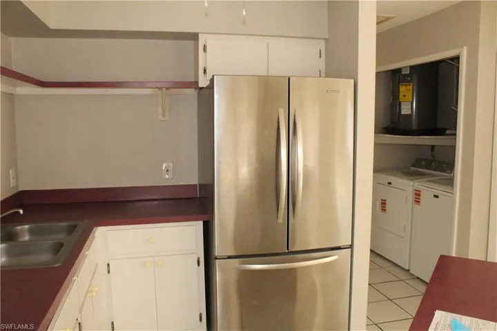 Kitchen with freestanding refrigerator, white cabinetry, washing machine and dryer, dark countertops, and light tile patterned floors