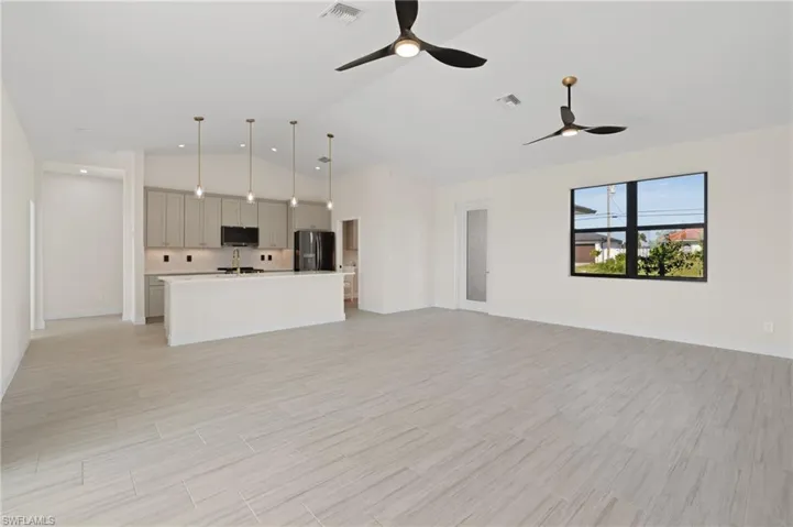 Unfurnished living room with light Italian tile floors, vaulted ceiling, and ceiling fan