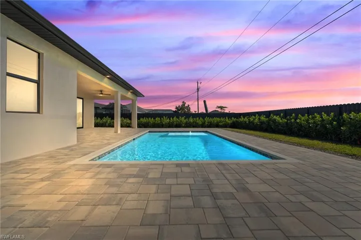 Pool at dusk featuring ceiling fan and a patio area