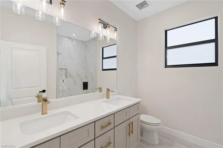 Bathroom with tiled shower, vanity, Italian tile flooring, and toilet