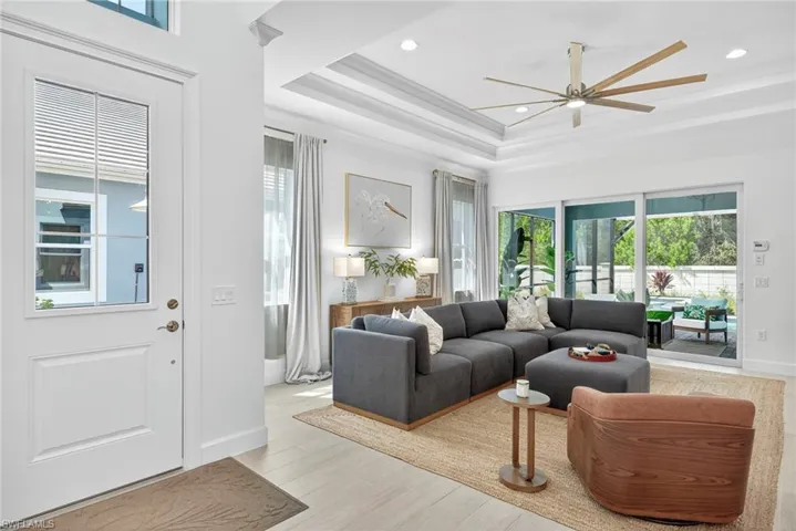 Living room featuring a raised ceiling, light wood-style flooring, ceiling fan, and recessed lighting