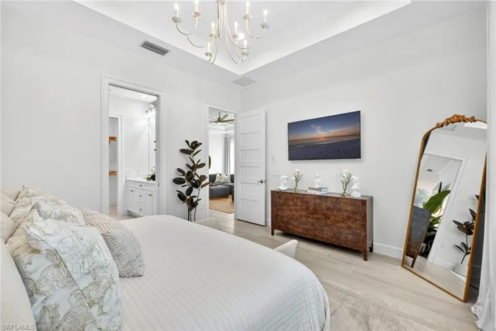 Bedroom featuring a chandelier, light wood-style flooring, a tray ceiling, and ensuite bath