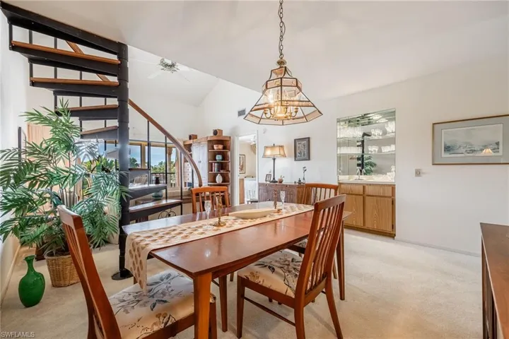 Dining space with ceiling fan with notable chandelier, light carpet, and vaulted ceiling