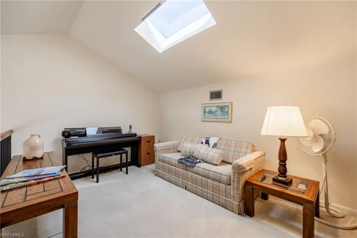Living room featuring lofted ceiling with skylight and light colored carpet