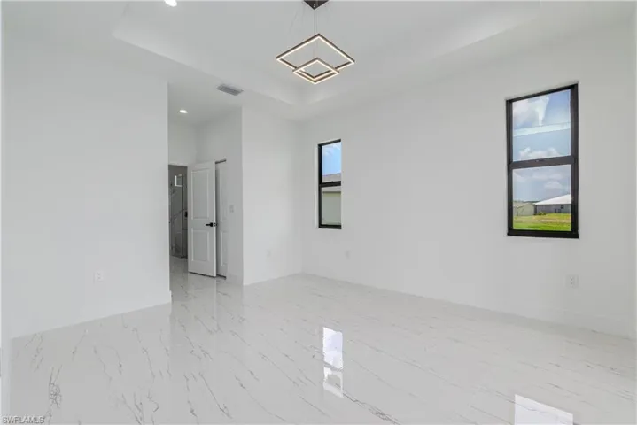Empty room with a raised ceiling, recessed lighting, and light marble finish flooring