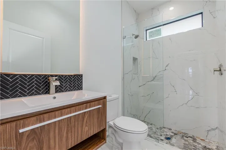 Full bath featuring decorative backsplash, a marble finish shower, and vanity