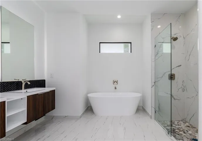 Bathroom featuring vanity, a marble finish shower, a freestanding bath, marble finish flooring, and recessed lighting