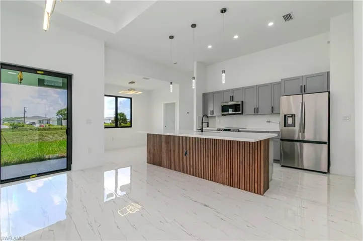 Kitchen with stainless steel appliances, open floor plan, light countertops, gray cabinets, and a kitchen island with sink