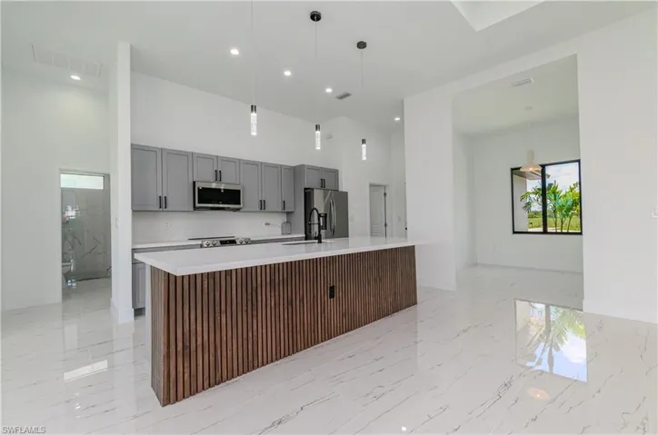 Kitchen with stainless steel appliances, gray cabinets, a towering ceiling, light countertops, and a large island