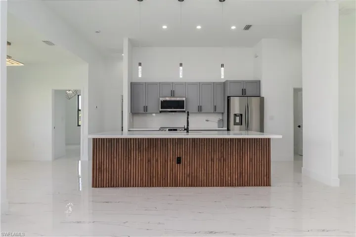 Kitchen featuring stainless steel appliances, gray cabinets, light countertops, a center island with sink, and light marble finish flooring