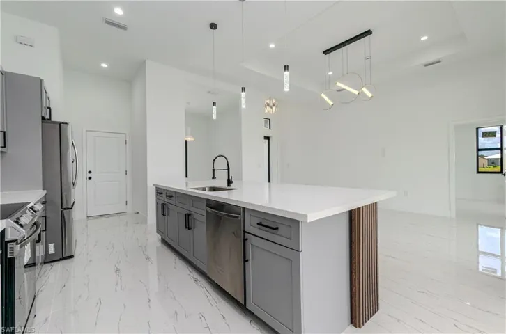 Kitchen with stainless steel appliances, gray cabinetry, light marble finish flooring, a tray ceiling, and recessed lighting
