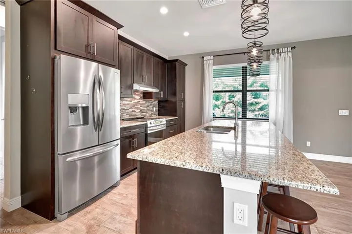 Kitchen with stainless steel appliances, light stone counters, espresso hued cabinetry and a double sink.