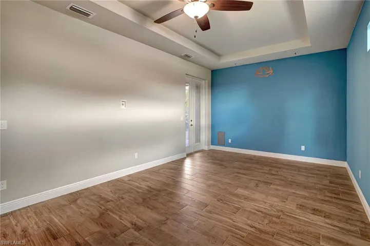 Large Master Bedroom featuring a coffered ceiling, wood plank tiled flooring, and ceiling fan and french doors that open to the private Lanai