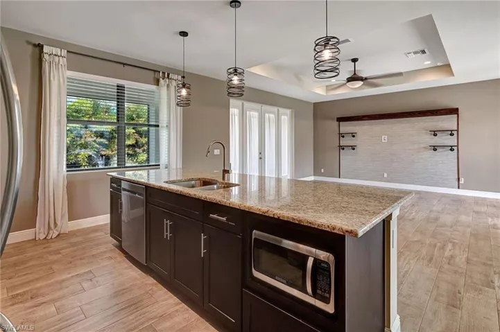 Kitchen featuring light stone counters, light wood plank tiled flooring, appliances with stainless steel finishes and a  island with sink