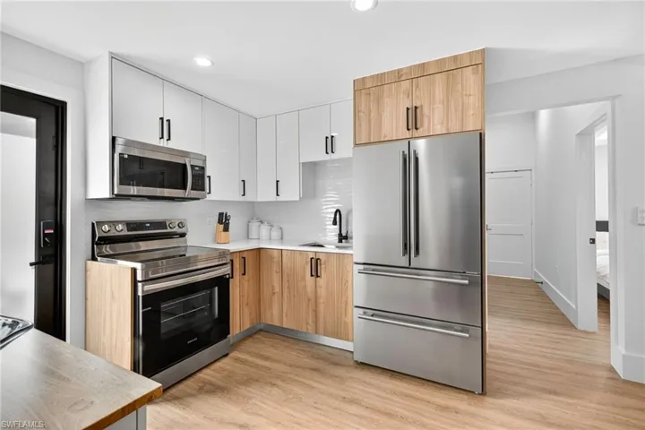 Kitchen with two tone cabinetry, stainless steel appliances, modern cabinets, light wood-style flooring, and decorative backsplash