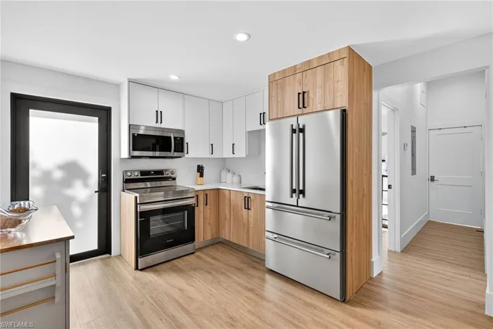 Two tone kitchen with light countertops, dual tone cabinets, stainless steel appliances, light wood-type flooring, and recessed lighting