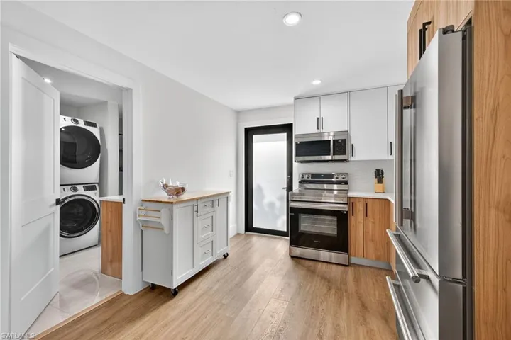 Two tone kitchen featuring two tone color scheme, stainless steel appliances, recessed lighting, light wood-style flooring, and stacked washer / drying machine