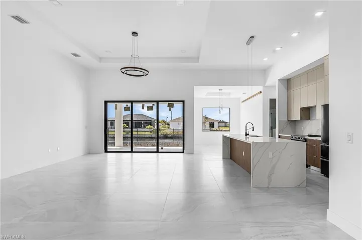 Kitchen with modern cabinets, hanging light fixtures, a tray ceiling, light stone counters, and recessed lighting