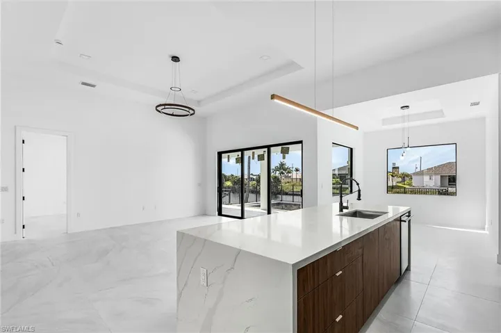Kitchen with a raised ceiling, modern cabinets, decorative light fixtures, dark brown cabinets, and open floor plan