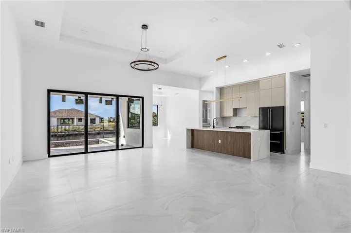 Kitchen with modern cabinets, decorative light fixtures, a tray ceiling, high quality fridge, and open floor plan