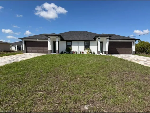 Prairie-style home with a front lawn, stucco siding, decorative driveway, and a garage