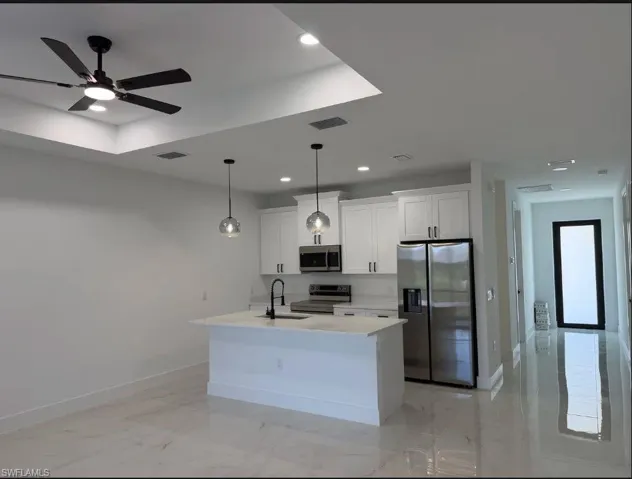 Kitchen featuring stainless steel appliances, white cabinetry, light marble finish flooring, a kitchen island with sink, and decorative light fixtures